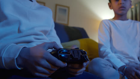 Nahaufnahme-Der-Hände-Von-Zwei-Kleinen-Jungen,-Die-Zu-Hause-Mit-Einer-Computerspielkonsole-Im-Fernsehen-Spielen-Und-Spät-In-Der-Nacht-Controller-Halten-6